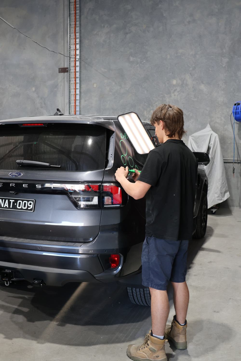 MRP technician marking dents for repair assessment with a light board — Redland Bay workshop